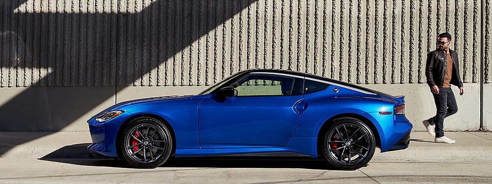 2024 Nissan Z in blue, side view parked in front of a concrete building, with a pedestrian doing a double-take